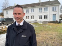 Bjørn Vevang med Rindal prestegård, som han og samboeren Anne leier, i bakgrunnen.