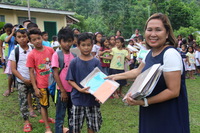 Edith Villamor handing out books to children who can now attend school, thanks to Sea and Sun Ministries International.